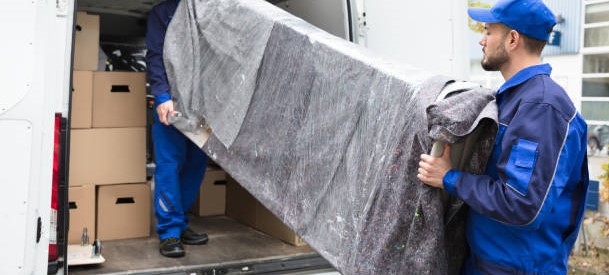 Two Young Delivery Men In Uniform Unloading Furniture From Vehicle
