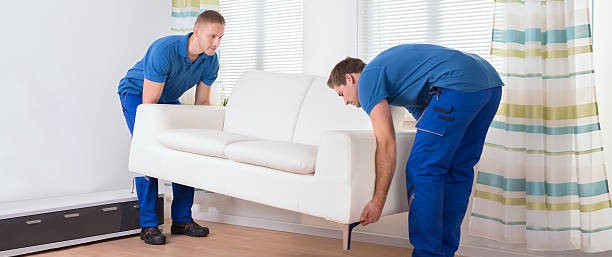 Full length of male movers placing sofa on hardwood floor at home