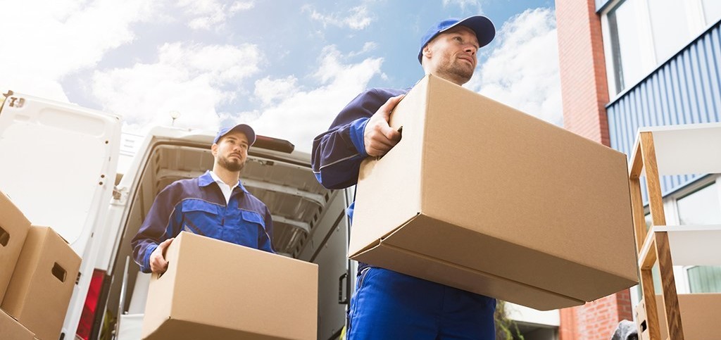Close-up Of Two Delivery Men Carrying Cardboard Box packing and shipping services in chicago